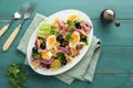 Tuna salad with pasta eggs potatoes olives red onions sauce in white plate on old turquoise wooden rustic table background Nicoise Royalty Free Stock Photo