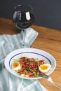 Tuna salad with vegetables, boiled eggs, cherry tomatoes and spices and one glass of red wine over wooden background Royalty Free Stock Photo