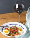 Tuna salad with vegetables, boiled eggs, cherry tomatoes and spices and one glass of red wine over wooden background Royalty Free Stock Photo