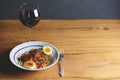 Tuna salad with vegetables, boiled eggs, cherry tomatoes and spices and one glass of red wine over wooden background Royalty Free Stock Photo