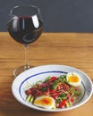 Tuna salad with vegetables, boiled eggs, cherry tomatoes and spices and one glass of red wine over wooden background Royalty Free Stock Photo