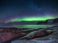 Tungeneset rocks and Aurora Borealis light. Stars trails and northern light. Reflections on the water surface. Senja islands, Norw