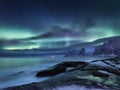 Tungeneset rocks and Aurora Borealis light. Stars trails and northern light. Reflections on the water surface. Senja islands, Norw