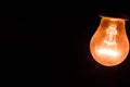 A tungsten light bulb is lit on a black background. Royalty Free Stock Photo