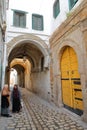 Typical cobbled and narrow street with colorful doors and arcades inside the historical medina of Tunis, and with two local women