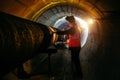 Tunnel worker examines pipeline in underground tunnel