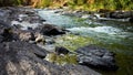 Turbulent river water rushing through the dark boulders and the rapids on a bright fall day. Royalty Free Stock Photo