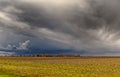 Turbulent skies loom over an expansive agricultural field