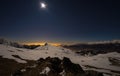 Turin city lights, night view from snow covered Alps by moonlight. Moon and Orion constellation, clear sky, fisheye lens. Italy.