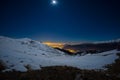 Turin city lights, night view from snow covered Alps by moonlight. Moon and Orion constellation, clear sky. Italy.