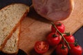 Turkey ham meat, fresh cherry tomatoes branch and loaf sliced bread on wooden cutting board, black textured background Royalty Free Stock Photo