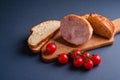 Turkey ham meat, fresh cherry tomatoes branch and loaf sliced bread on wooden cutting board, blue minimal background Royalty Free Stock Photo