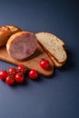 Turkey ham meat, fresh cherry tomatoes branch and loaf sliced bread on wooden cutting board, blue minimal background Royalty Free Stock Photo