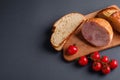 Turkey ham meat, fresh cherry tomatoes branch and loaf sliced bread on wooden cutting board, grey minimal background Royalty Free Stock Photo