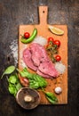 Turkey steak on a cutting board with mushrooms and green peppers tomatoes and lemon garlic on wooden rustic background top view