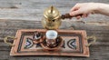 Turkish coffee. Pouring Turkish coffee into vintage cup on wooden background. Pouring Turkish coffee into traditional embossed Royalty Free Stock Photo