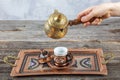 Turkish coffee. Pouring Turkish coffee into vintage cup on wooden background. Pouring Turkish coffee into traditional embossed Royalty Free Stock Photo