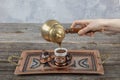 Turkish coffee. Pouring Turkish coffee into vintage cup on wooden background. Pouring Turkish coffee into traditional embossed Royalty Free Stock Photo