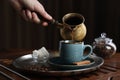 Turkish coffee. Woman pouring brewed beverage from cezve into cup at wooden table, closeup Royalty Free Stock Photo