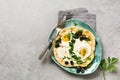 Turkish eggs flatbread with yoghurt, cheese, olives, spinach and red pepper on ceramic vintage plate on gray old background.