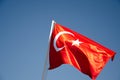 The Turkish flag flies in the wind on a flagpole against the blue sky. The national red and white flag of the country of Turkey is Royalty Free Stock Photo