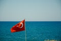 The Turkish flag flies in the wind on flagpole against the blue sky and the sea. The national red and white flag of the country of Royalty Free Stock Photo