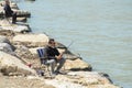 Turkish man fishermen sitting on a small folding chair on stone coast and fish with fishing rod in the sea bay Royalty Free Stock Photo