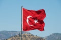 Turkish National flag at the flagpole waves over a hill with a blue summer sky at the background in Bodrum, Turkey.