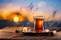 Turkish tea served in tulip-shaped glass on a small saucer and blurred purple and orange sunset in the field at the background Royalty Free Stock Photo