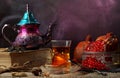 Turkish tea, the teapot is on a big book, there is steam, a national Turkish cup with tea and a vase with a ripe garnet.