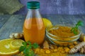 Turmeric juice in a bottle, lemon, orange and turmeric powder on a wooden background