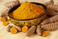 Turmeric powder in asian bowl with fresh turmeric roots selective focus on turmeric powder