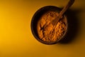 Turmeric powder in wooden bowl with wooden spoon on yellow background. Closeup view. Low key image with copy space