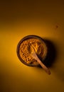 Turmeric powder in wooden bowl with wooden spoon on yellow background. Top view. Low key image with copy space