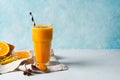 Turmeric smoothie in glass with ingredients, turmeric powder, ginger and spice on blue