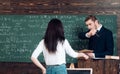 Turn back girl passing book to her professor standing at rostrum. Young teacher staring at his beautiful female student Royalty Free Stock Photo