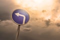 Turn left ahead sign, blue round roadside traffic signage, against the dramatic sky Royalty Free Stock Photo