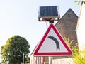 Turn left warning road sign supplied by solar energy through a solar panel Royalty Free Stock Photo