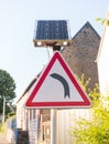 Turn left warning road sign supplied by solar energy through a solar panel Royalty Free Stock Photo