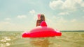 Turned back girl floating away on pink inflatable mattress