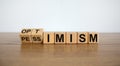 Turned a cube and changed the expression `pessimism` to `optimism`. Beautiful wooden table, white background. Business concept