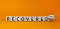 Turned a cube and changed the words `recovered no` to `recovered yes` on wooden cubes. Beautiful orange background, copy space
