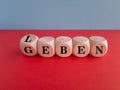 Turned a dice and changes the German word leben to geben. Beautiful red table, blue background. Royalty Free Stock Photo