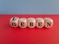 Turned a dice and changes the German word leben to geben. Beautiful red table, blue background.