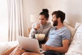 Turning their bedroom into a cinema. a happy young couple using a laptop and eating popcorn while relaxing on the bed at Royalty Free Stock Photo