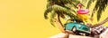 Turquoise blue retro car with pink flamingo and summer travel accessories under the palm tree on yellow background
