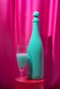 Turquoise champagne wine bottle with crystal glass on red the podium. Magenta curtains background