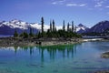 Turquoise coloured lake with trees on the island and snow mountains