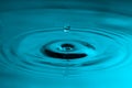 Perfect water drop splashing into smooth water causing ripples Royalty Free Stock Photo