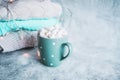 Turquoise cup, mug of hot drink with white marshmallow, stack of knitted clothes. Winter cozy still life